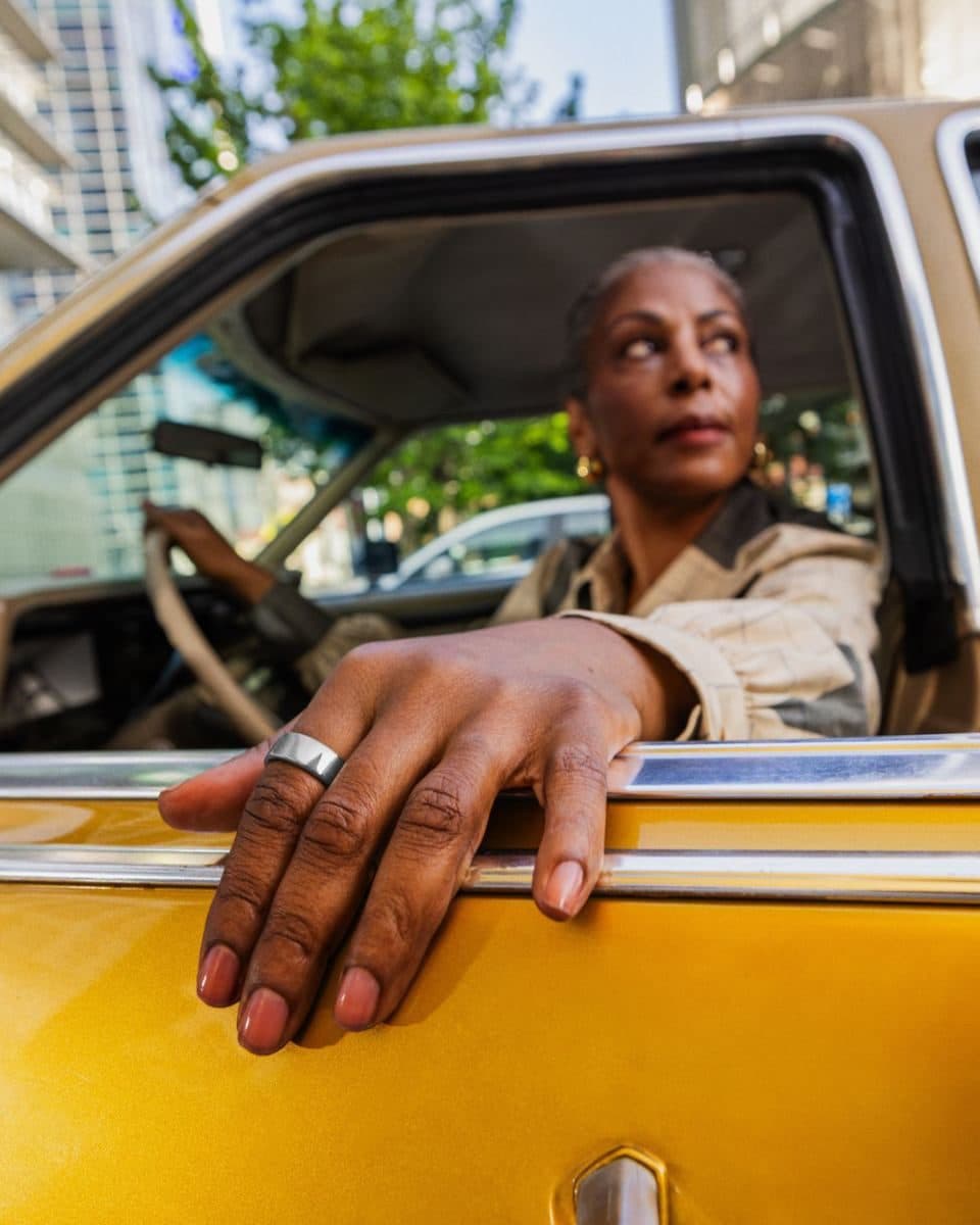 Eine Frau lehnt sich aus einem Taxifenster und trägt einen Oura Ring